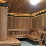 Inside of wooden sauna with decorative wooden railings and lit ceiling.