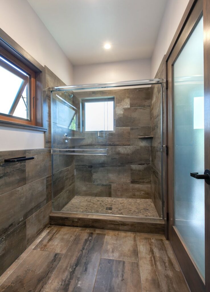 Walk in glass door shower with attractive stone tiling and wood floors. An open window lets in light.