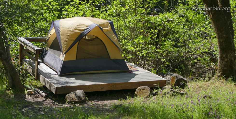 A tent sits on a tent sized deck near the creek in the meadow area.