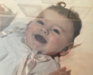 A laughing baby, Sue as a baby, with a little curl on their head from an original photo.